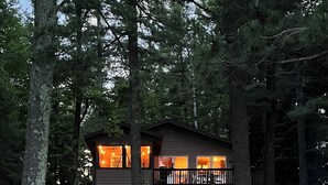 A cabin with a wooden deck leading to a small pond, surrounded by trees. - Beautiful 3 bed/2bath updated cabin w sandy swimmable frontage & great fishing (Eagle River)