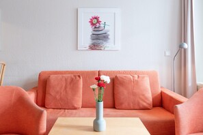 Ein Wohnzimmer mit einer Couch, einer Blumenvase und einem gerahmten Bild an der Wand.