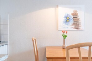 Ein Holztisch mit Blumen in einer Vase, ein Stuhl und ein gerahmtes Bild an der Wand.
