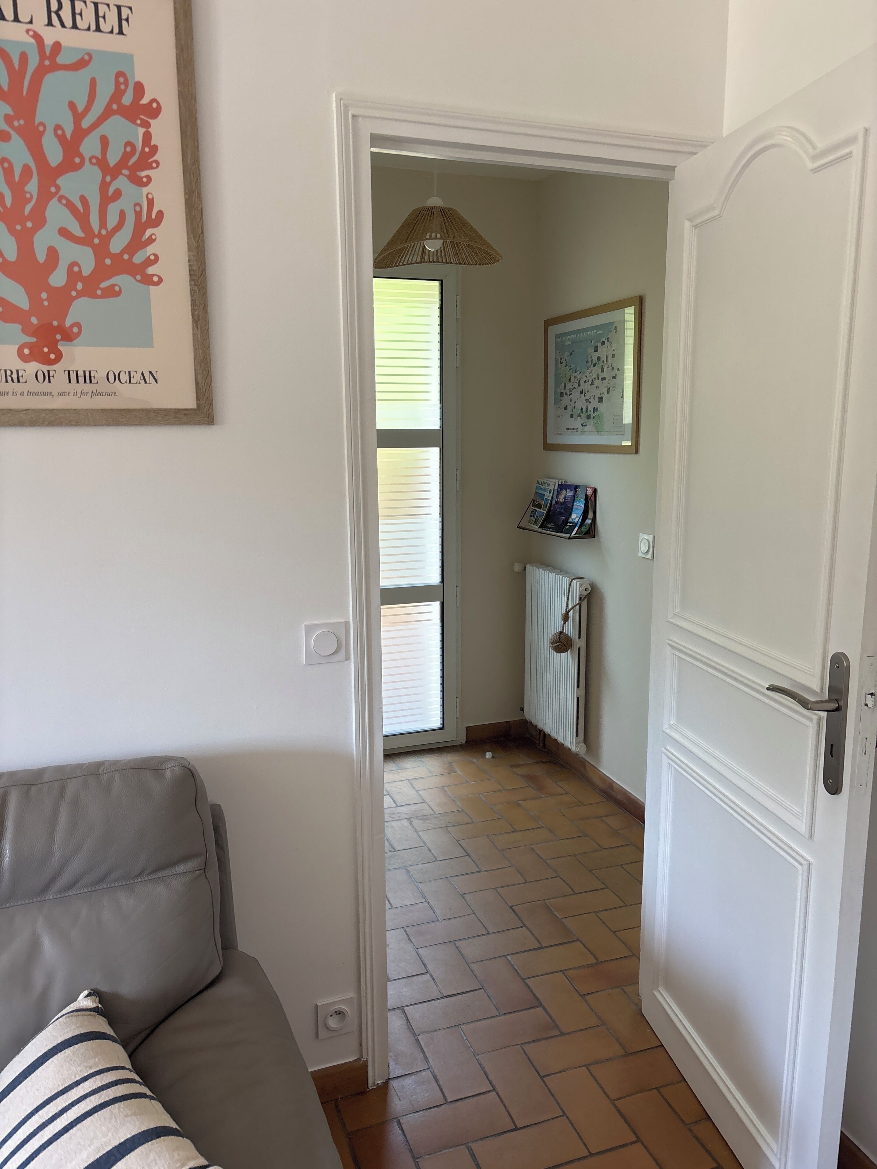 A room with a door leading to a hallway, a framed picture on the wall, and a tiled floor.