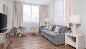 A modern living room with a grey sofa, two wicker chairs, a TV on a wooden stand, and a white side table with a lamp. - Marriott Vacation Club hotel suite in gorgeous Miami Beach with fitness room (Miami Beach)