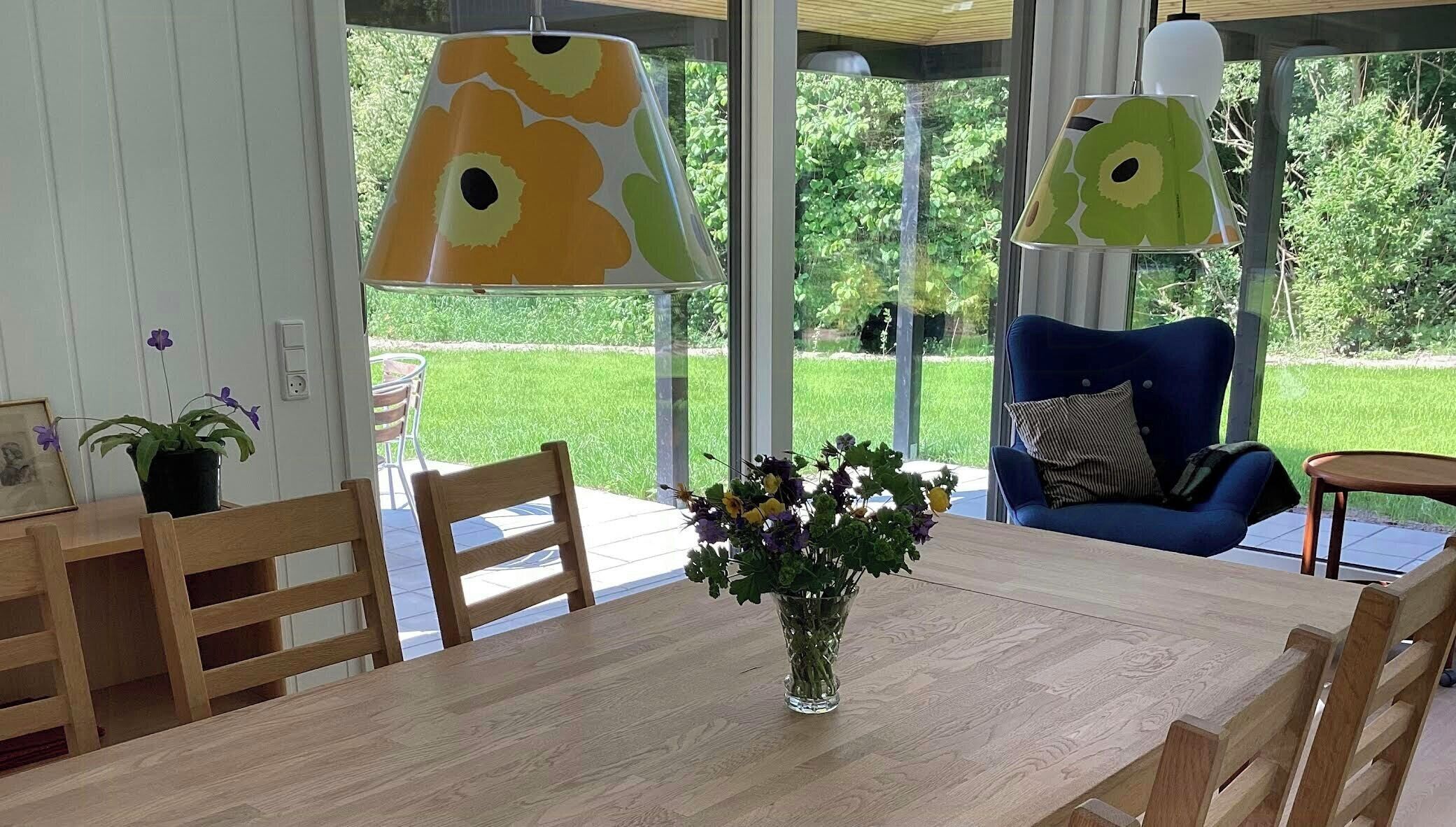 Een eethoek met een houten tafel, stoelen, een vaas met bloemen en een blauwe stoel met kussen.