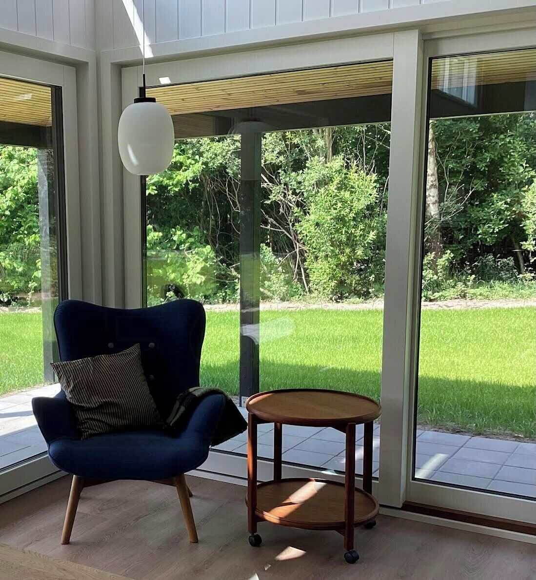 A room with a blue chair, a small round table, and a hanging light fixture.