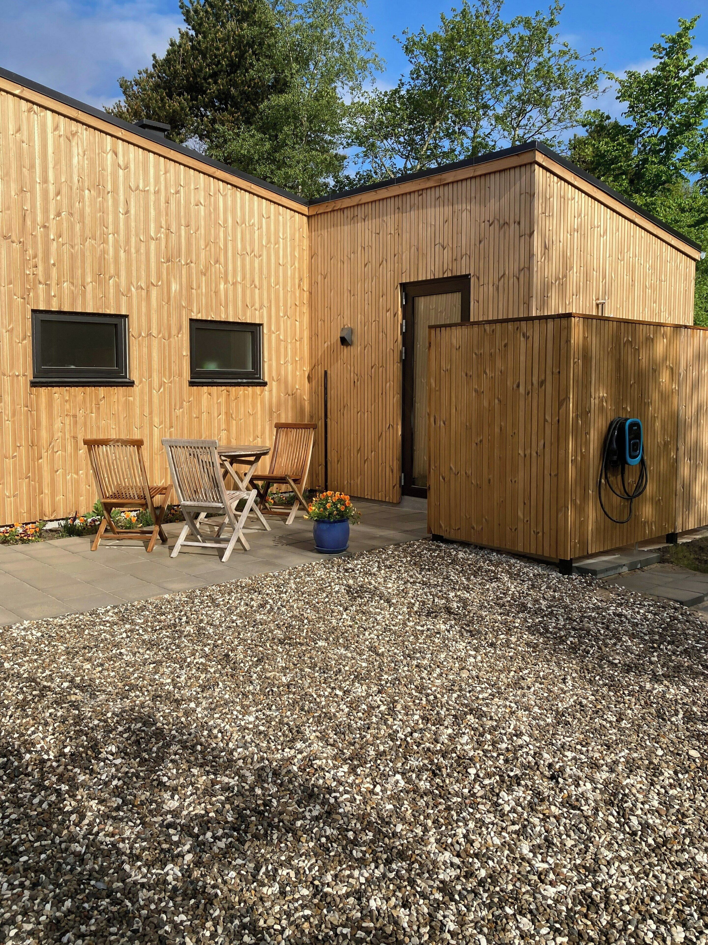 A wooden building with two windows and a door, a gravel patio, and two wooden chairs.