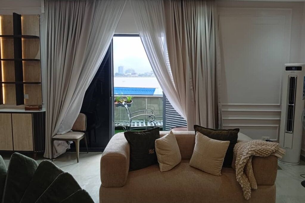 A living room with a sofa, a chair, a bookshelf, and a view through a window with curtains.