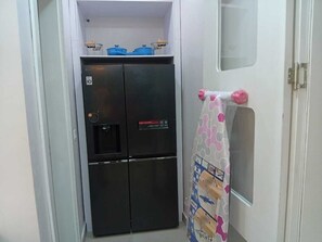 Eine kompakte Küche mit einem schwarzen Kühlschrank, einer kleinen Ablage mit blauen Behältern und einem Handtuch an der Tür.