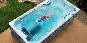 A rectangular hot tub with a person swimming inside, surrounded by a grassy area and a stone pathway. - Enchanting 3500sq Mansion Pool Jacuzzi Minigolf 12 Guests Hard Rock Casino Beach (Hollywood)