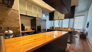 A modern kitchen with a wooden countertop, stainless steel appliances, and a brick accent wall. - Downtown Delight: Cozy + Chic 2 Bedroom Loft in Downtown Macon (Macon)