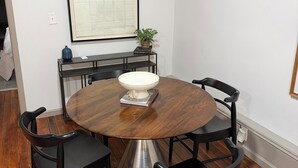 A dining area with a round table, four chairs, a white bowl, a framed picture, and a small plant on a console table. - Downtown Delight: Cozy + Chic 2 Bedroom Loft in Downtown Macon (Macon)