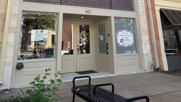 A building with a large window, a door with a sign, and a flag. - Downtown Delight: Cozy + Chic 2 Bedroom Loft in Downtown Macon (Macon)
