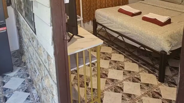 Een slaapkamer met een bed, gordijnen, een nachtkastje en een betegelde vloer.