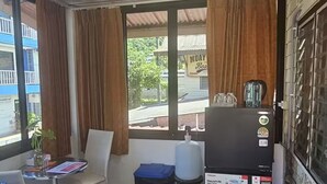 Een kleine kamer met een betegelde vloer, een tafel met stoelen, een koelkast en een raam met gordijnen.