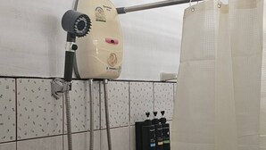 Een douchegedeelte met een handdouche, een douchegordijn en een bedieningspaneel aan de muur.