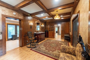 A spacious room with wooden floors, a large rug, a rocking chair, a fireplace, and a mirror on the wall.