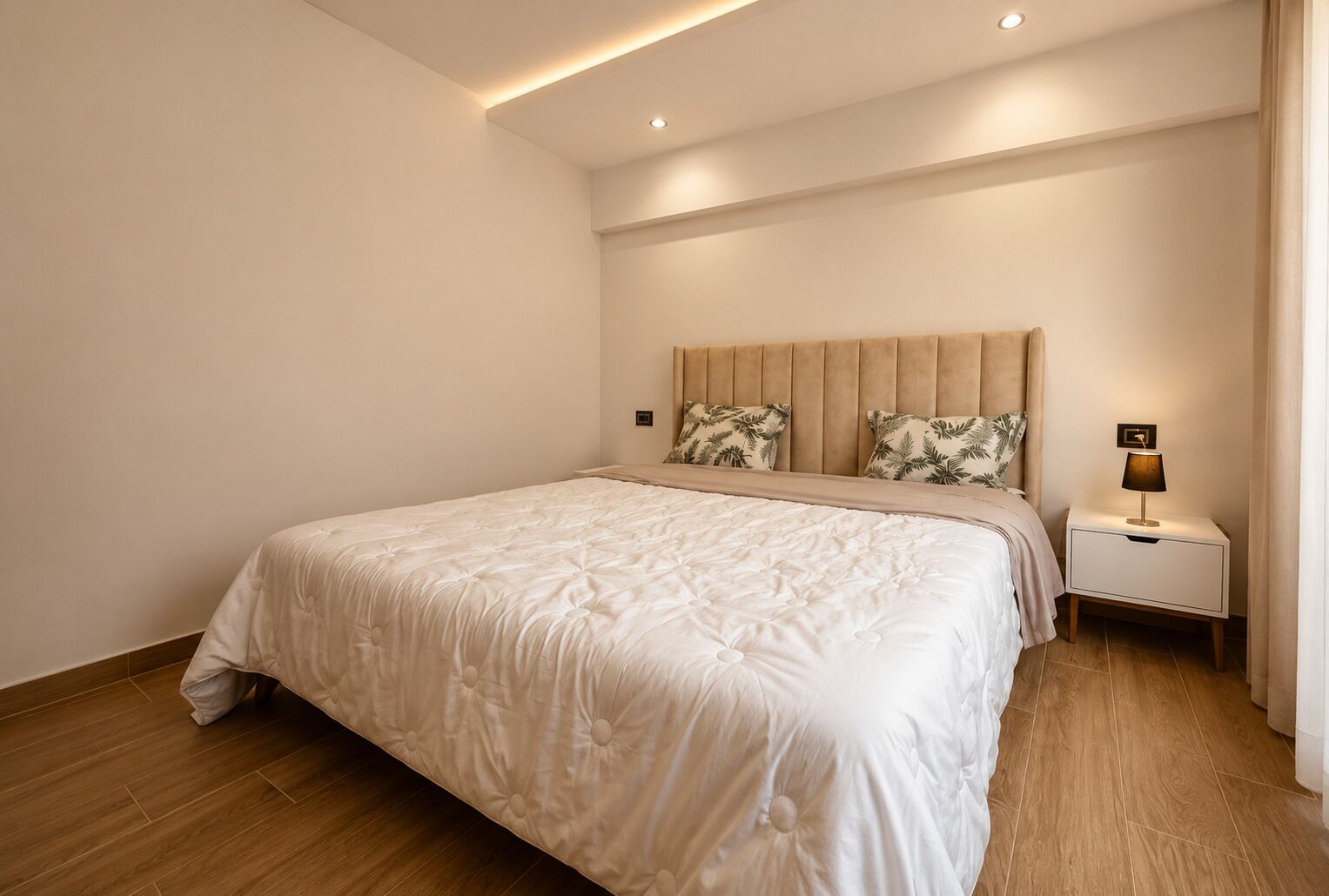 Ein Schlafzimmer mit einem großen Bett, einem Nachttisch mit Lampe und einem Kopfteil mit dekorativen Kissen.