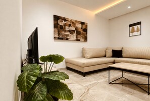 A modern living room with a sectional sofa, a flat-screen TV, a coffee table, and a large abstract painting on the wall. - Charming House (Tunis)