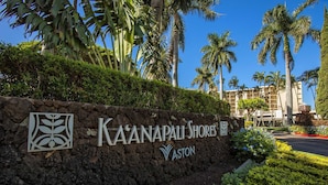 Letrero de Ka'anapali Shores con un muro de piedra, palmeras y un edificio al fondo.