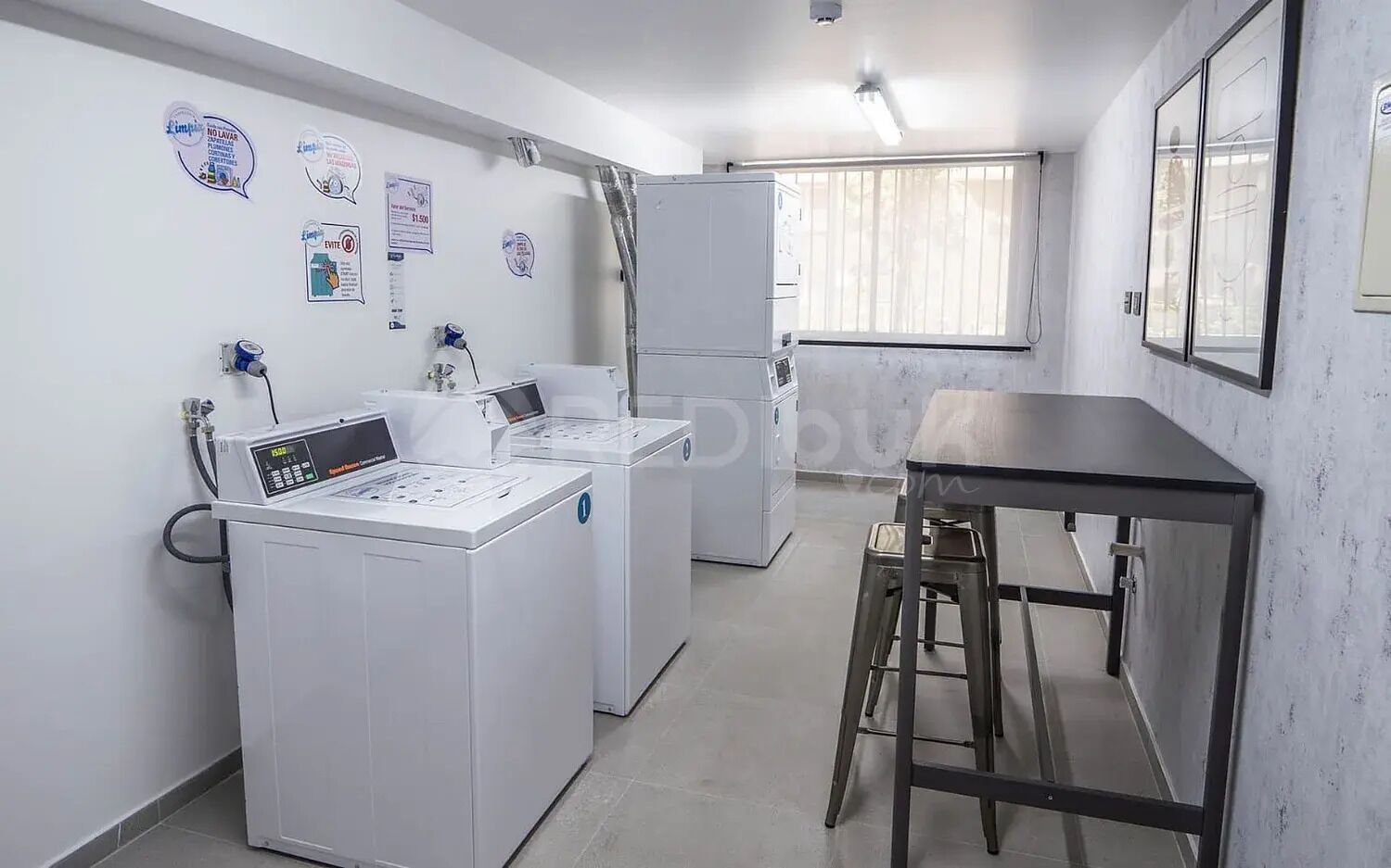 A laundry room with two washing machines, a table, and a stool.