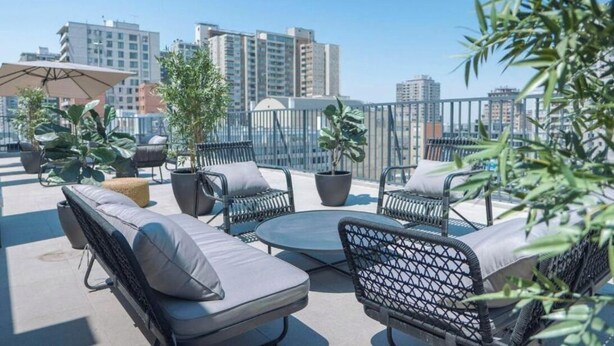 A rooftop terrace with outdoor seating, potted plants, and a city skyline in the background. - Rbk Dpto GIM-3 personas-Lavanderia-WIFI (Santiago)