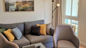 Un salon avec un canapé gris, une table basse en verre, un lampadaire et une grande fenêtre.