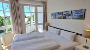 Une chambre d’hôtel avec un grand lit, deux tables de chevet, une fenêtre avec des rideaux et trois tableaux encadrés accrochés au mur.