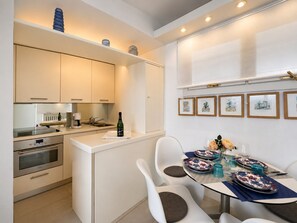 Uma cozinha moderna com eletrodomésticos embutidos, uma área de refeições com mesa de vidro e quadros nas paredes.