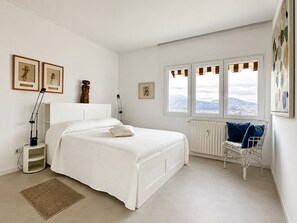 Quarto com cama, cadeira, radiador e janela com vista.