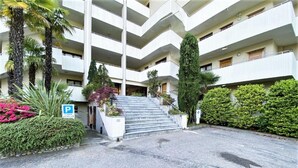 Ein mehrstöckiges Gebäude mit Parkplatz, Treppe zum Eingang und umliegender Bepflanzung.