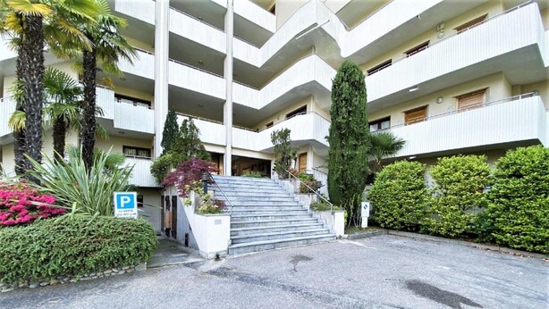 Ein mehrstöckiges Gebäude mit Parkplätzen, einer Treppe zum Eingang und umgebender Bepflanzung.