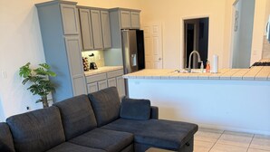 Una sala de estar moderna con un sofá seccional, una mesa de centro y una zona de cocina con armarios y un refrigerador.