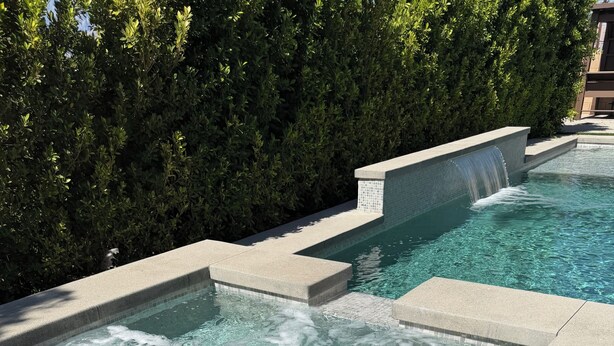Una piscina con cascada y borde de azulejos.