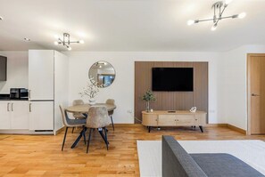 Ein modernes Wohnzimmer mit Essbereich, einem an einer Holzpaneelwand montierten Flachbildfernseher und einer Deckenleuchte.