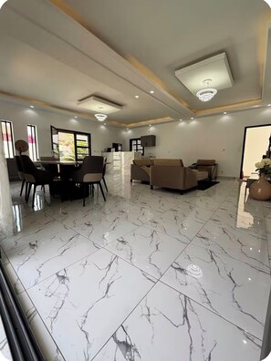 Una sala de estar moderna con piso de mármol, un juego de sofá, un comedor con sillas y una cocina al fondo.