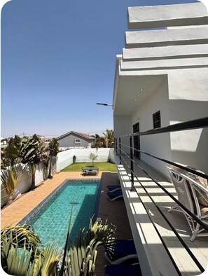 Zona de piscina con una piscina azul cristalina, una pequeña mesa y sillones de descanso.