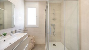 A modern bathroom with a glass-enclosed shower, a large mirror, and a beige tiled floor. - LXR Totally Refurbished Riviera 2-Bedroom (AN)