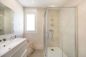 Ein modernes Badezimmer mit einer in Glas gefassten Dusche, einem großen Spiegel und einem beige gefliesten Boden.