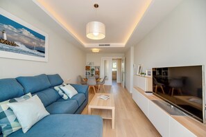 Ein modernes Wohnzimmer mit einem blauen Sofa, einem Couchtisch, einem Fernseher und einem Essbereich mit Stühlen und einem Tisch.