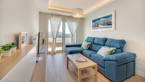 A modern living room with a blue sofa, a wooden coffee table, and a city view through large windows. - LXR Totally Refurbished Riviera 2-Bedroom (AN)
