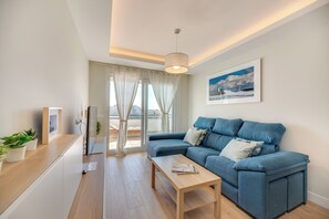 Ein modernes Wohnzimmer mit einem blauen Sofa, einem Holztisch und Blick auf die Stadt durch große Fenster.