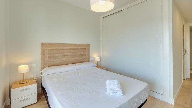 A neatly made bed with a wooden headboard, a bedside lamp, and a folded towel on the bed. - LXR Totally Refurbished Riviera 2-Bedroom (AN)