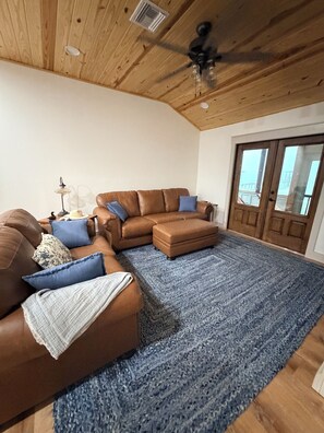 Ein Wohnzimmer mit einem braunen Ledersofa, einem blauen Teppich und einem Deckenventilator.