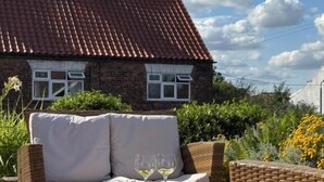 Een bakstenen huis met een dak van rode tegels, een rieten zithoek en een tafel met een glas wijn.