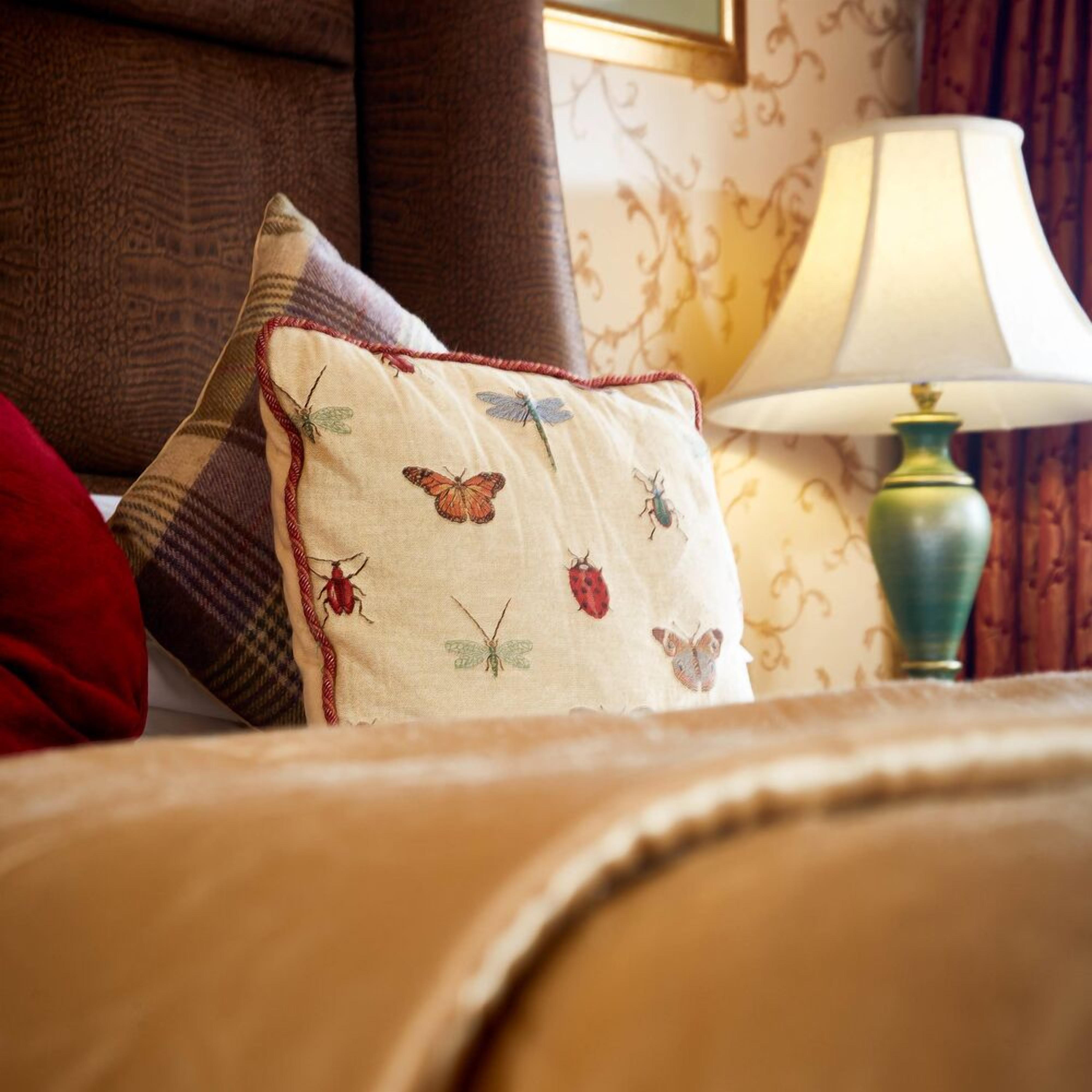 Una cama con un cojín estampado, una lámpara y una pared con un diseño decorativo.