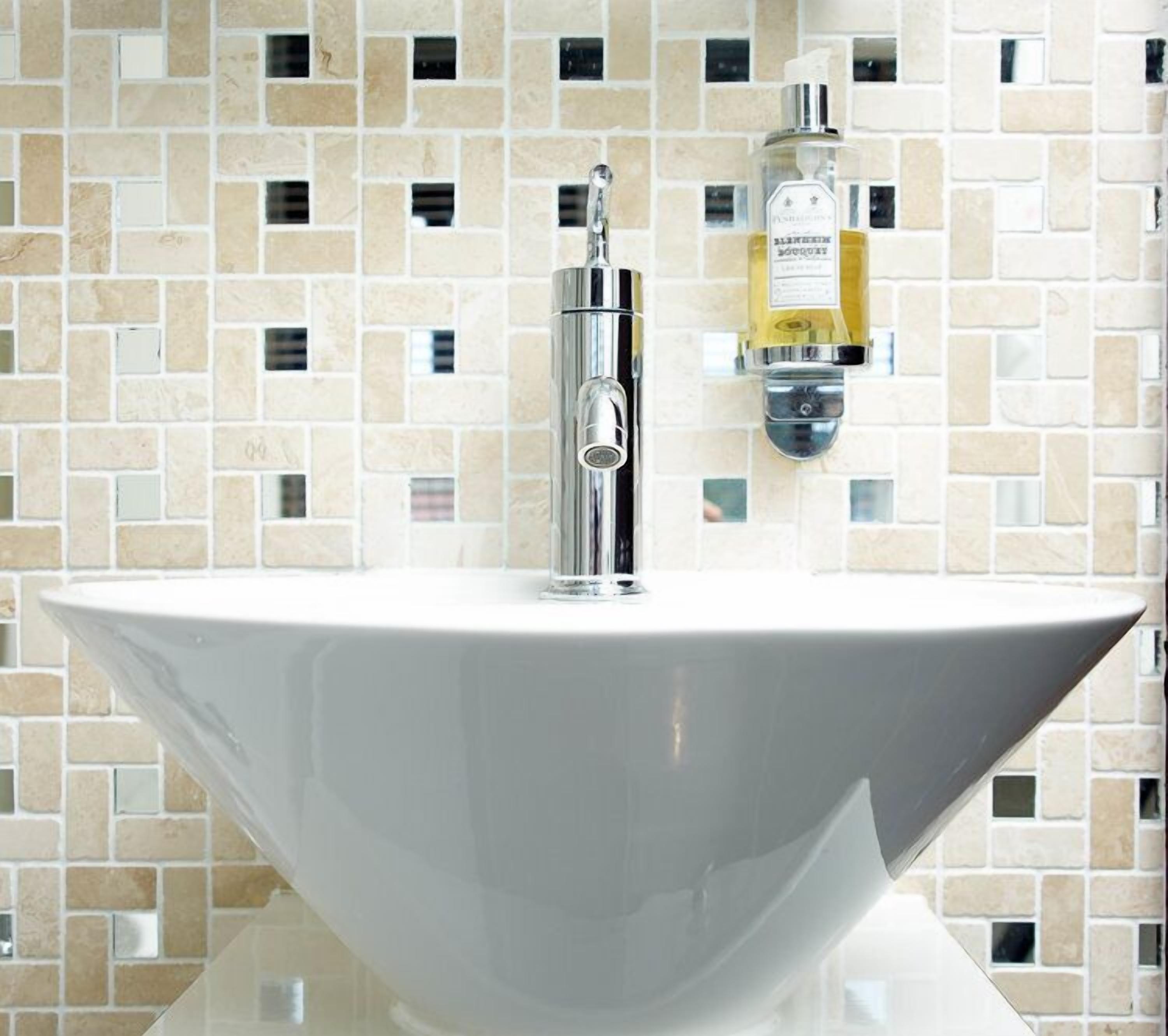 A white basin sink with a chrome faucet and a bottle of liquid soap on the wall.