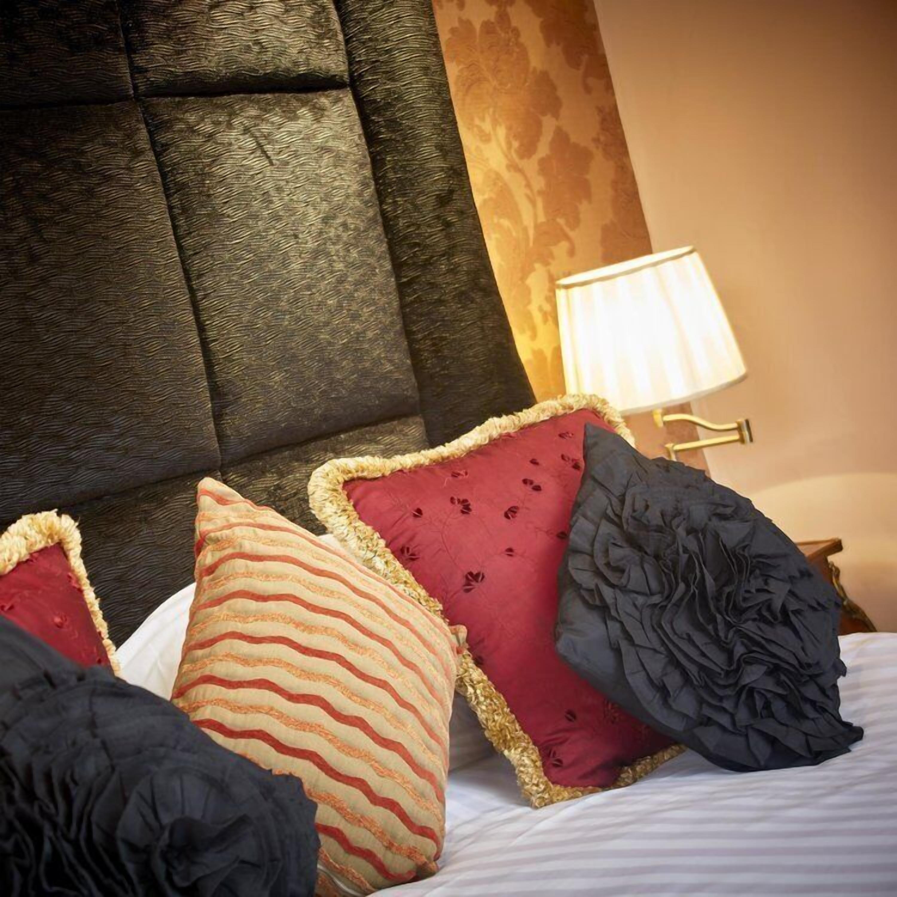 A bed with a tufted headboard, multiple pillows, and a bedside lamp.
