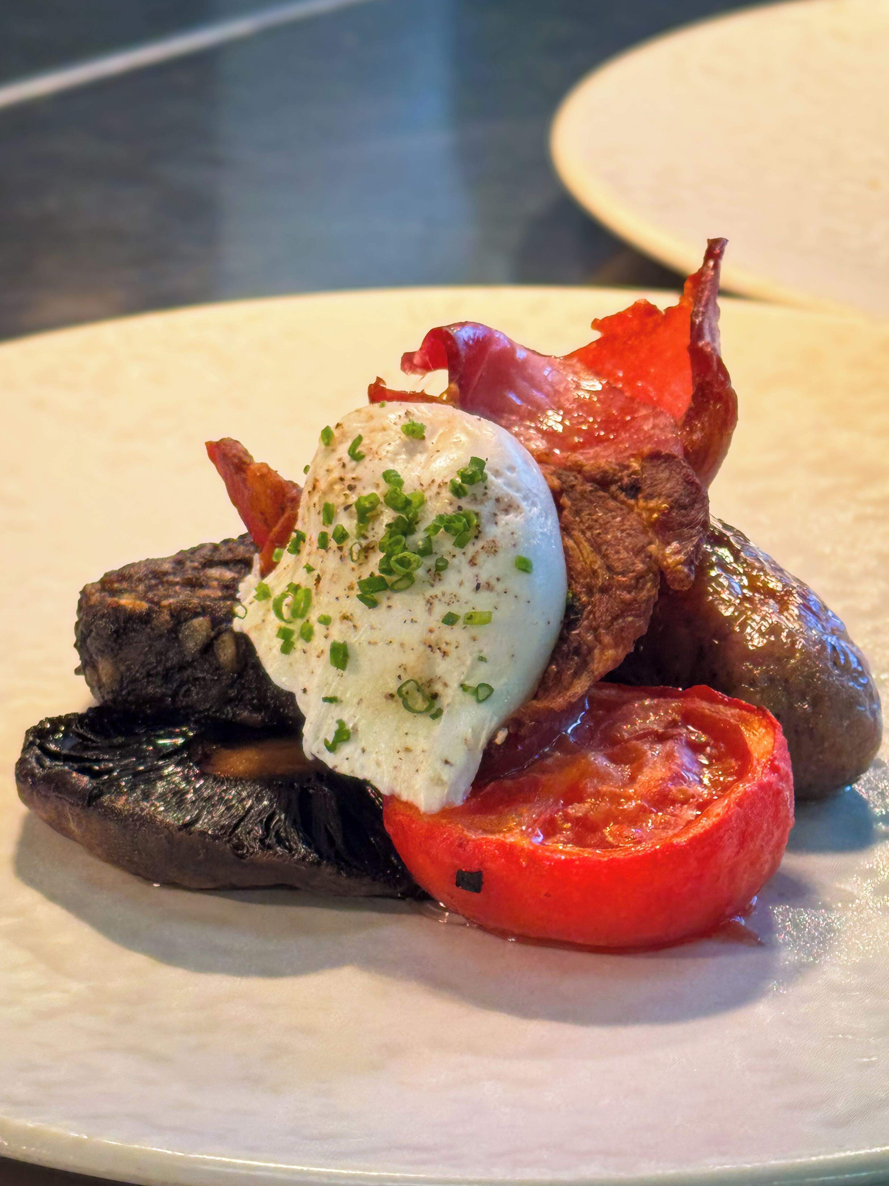 A plate with a grilled meat, a slice of tomato, and a poached egg.