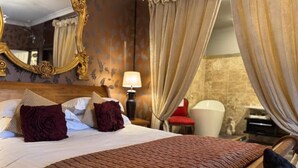 Een hotelkamer met een groot bed, een houten hoofdbord, een spiegel, een nachtkastje, een lamp en uitzicht buiten door gordijnen.