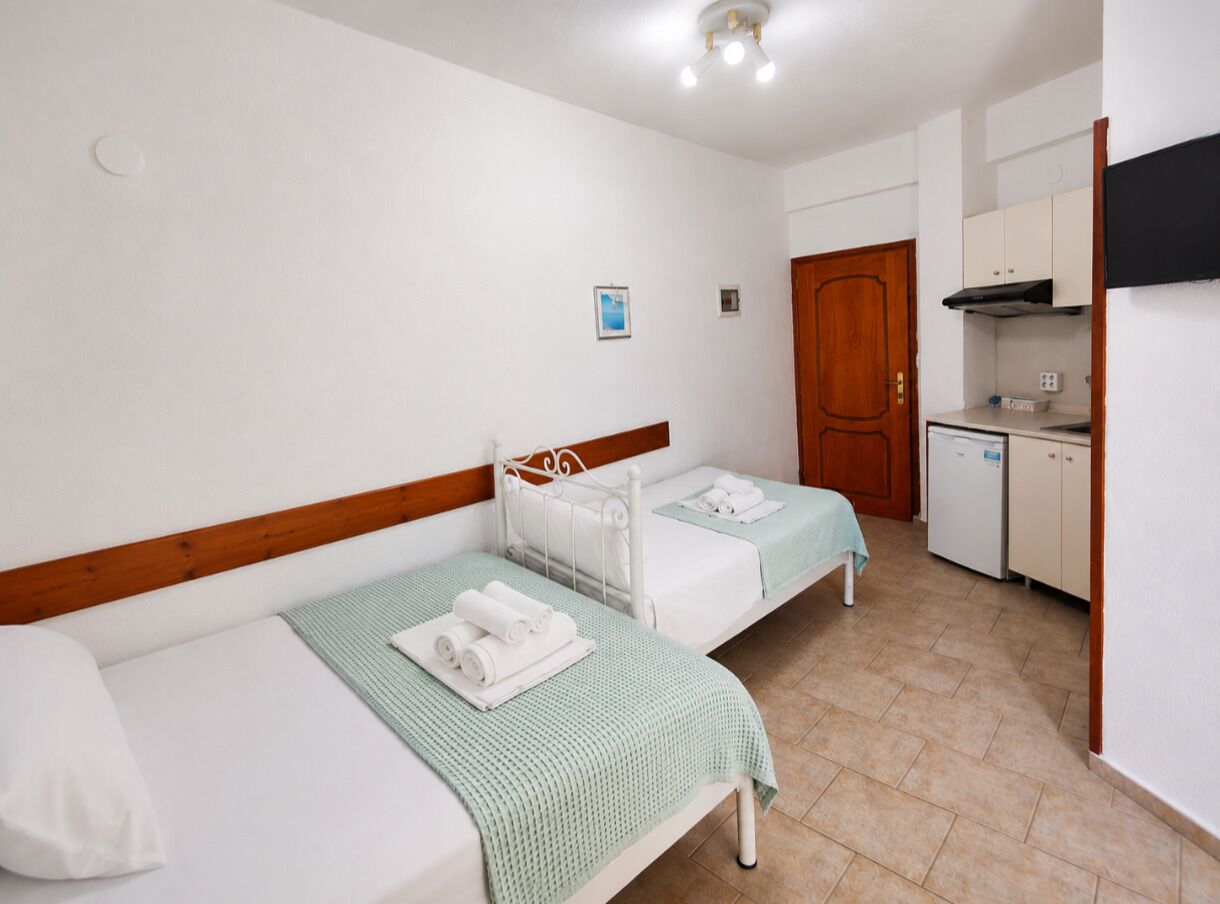 A room with two beds, a kitchenette, and a door.