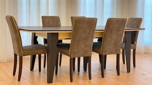 Ruokapöytä kuudella tuolilla, puulattia ja ikkuna, jossa on verhot.
