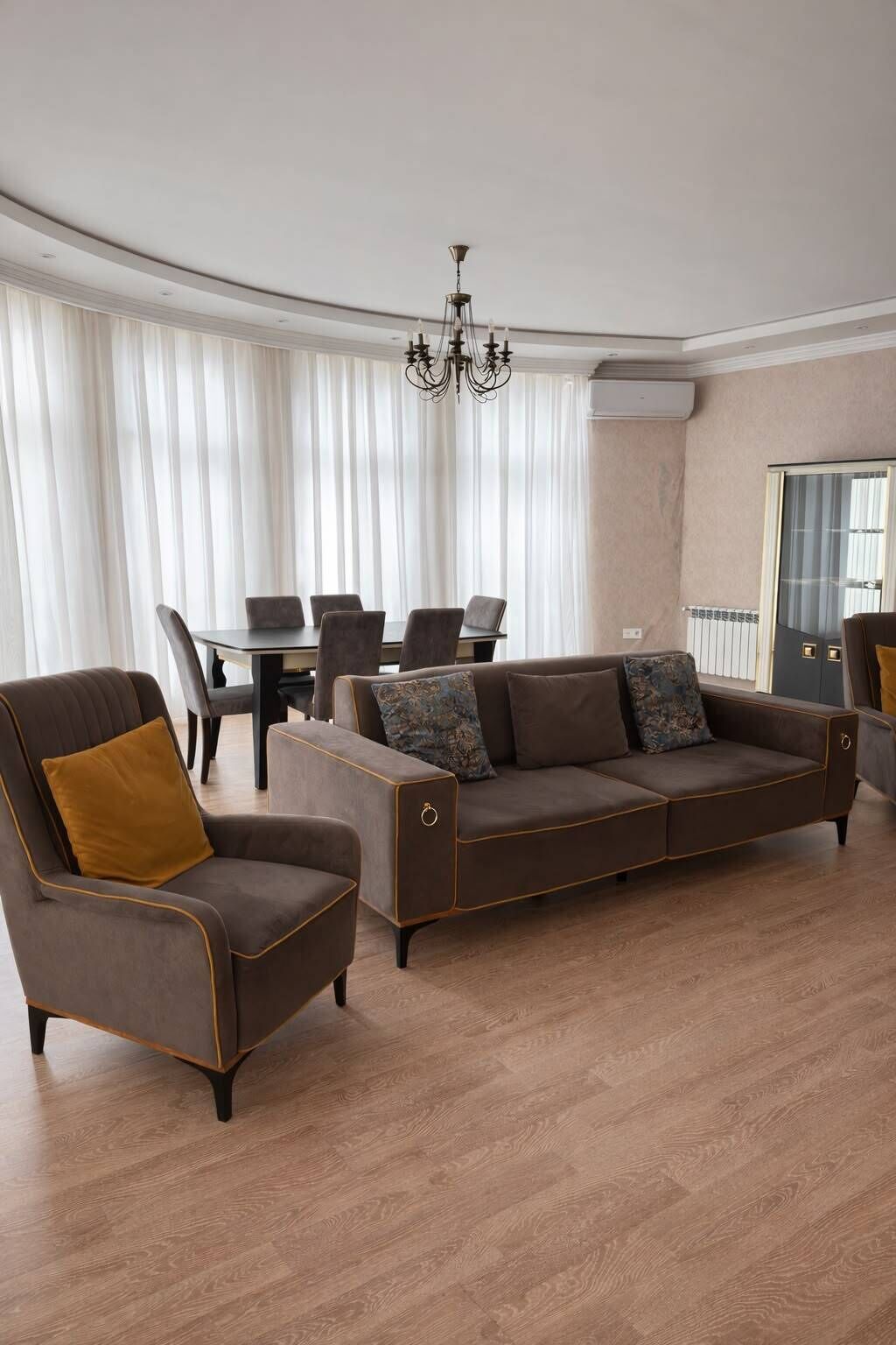 Ein modernes Wohnzimmer mit einer braunen Couch, einem braunen Sessel, einem Esstisch mit Stühlen und einer Pendelleuchte.